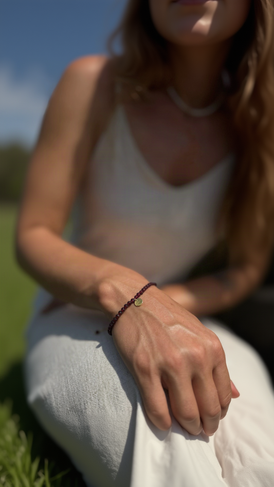 A close-up lifestyle shot of a woman outdoors wearing a red garnet bracelet with a small gold circular Sephina charm.