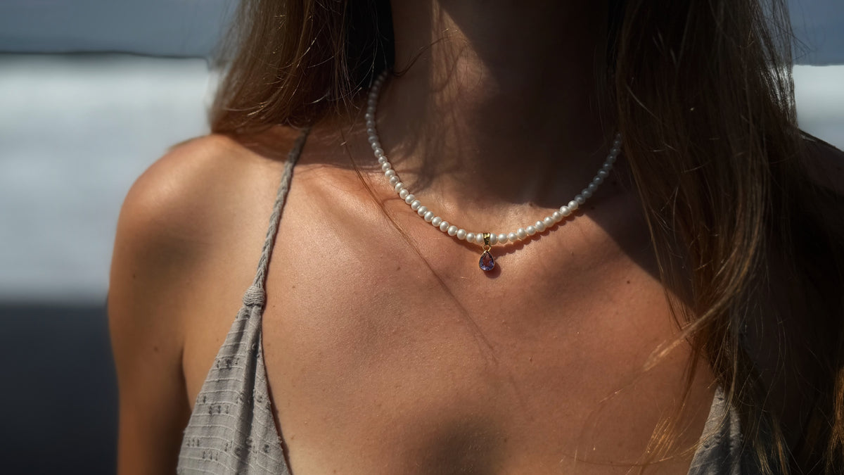 A close-up lifestyle shot of a woman wearing a delicate Sephina freshwater pearl necklace with a amethyst pendant.