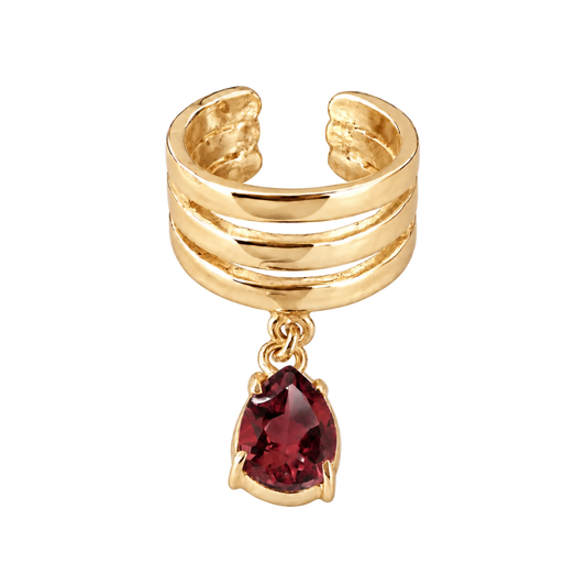 A gold-plated triple-band cuff ring featuring a dangling pear-cut red gemstone, shown on a light gray background.