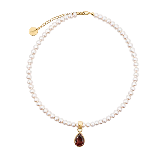 A delicate pearl necklace with a gold chain extender and a teardrop-shaped dark red gemstone pendant, displayed on a clean white background.