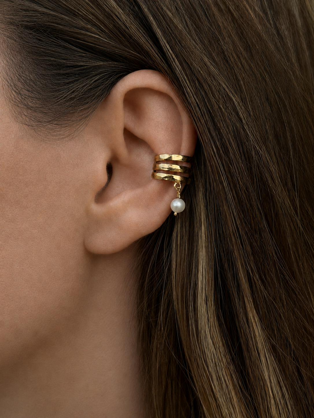 A close-up of a model's ear wearing a Sephina gold ear cuff with a dangling freshwater pearl.