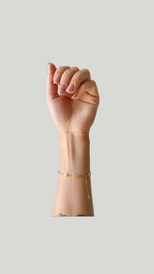 A gold chain bracelet with a 6 freshwater pearl, shown worn on a person's wrist against a solid light gray background.