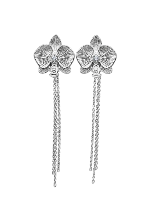 A pair of silver orchid drop earrings with textured petals and dangling chain tails, shown against a solid black background.